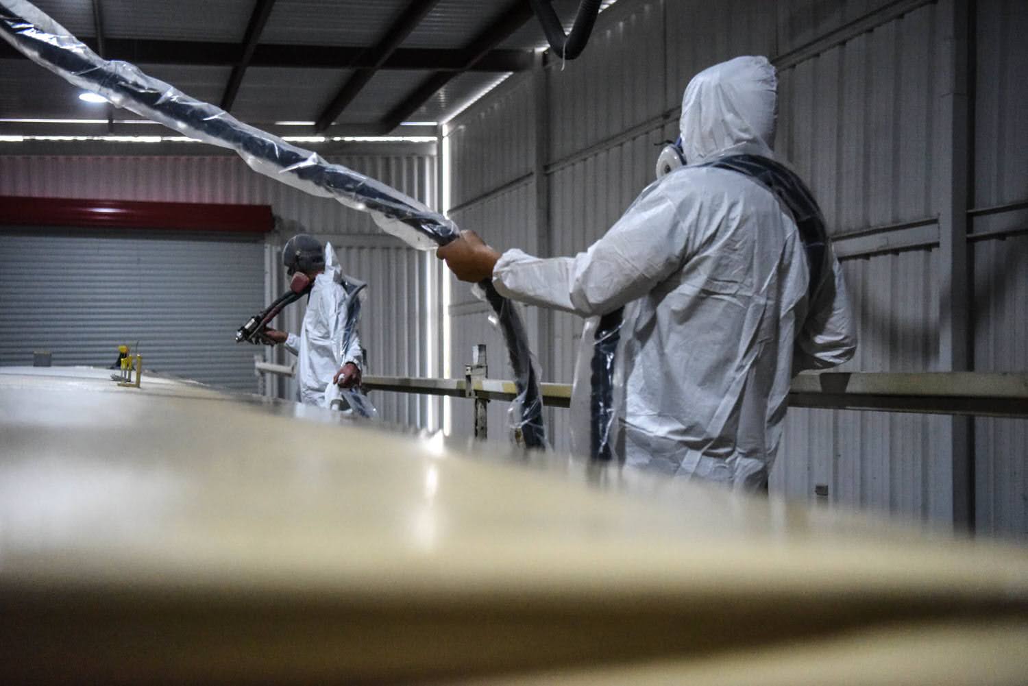 Two applicators spraying polyurea on an RV roof inside a shop